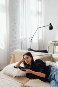 Woman cozied up on a couch with a remote control in hand. 