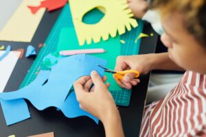 Child using kids scissors to cute pieces of colorful construction paper