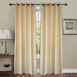 A well-lit interior room view showing a pair of floor-length, thick beige or cream-colored grommet curtains hanging from a dark metal rod. The curtains are drawn closed to block out light from a multi-pane window, flanked by a small wooden side table and a traditional table lamp to the left.